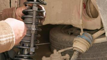 The calloused hands of a mechanic twist the coil spring ties with a wrench during DIY car repairs. video