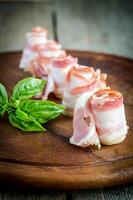 Rolled bacon strips on wooden board photo