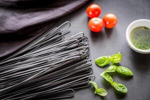 Raw black pasta with basil and tomatoes photo