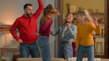 Caucasian happy family funny carefree parents children playful dancing active little girls kids daughters jumping on sofa celebrate weekend moving home party holiday laugh fun enjoy music dance jump video