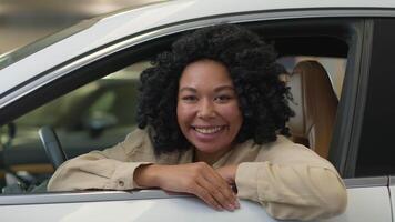 Happy smiling African American woman girl lady female driver sit inside modern electric car choosing buying new automobile in dealership salon store joyful cheerful client buyer rent vehicle purchase video