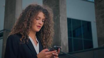 caucasien fille femelle entrepreneur femme d'affaires Jeune affaires femme en marchant dans ville tenir mobile téléphone à la recherche à téléphone intelligent écran répondre message navigation téléphone portable l'Internet numérique réseau en plein air video