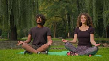 Yoga sport morning meditation multiracial couple Arabian Indian man Caucasian woman sit in lotus pose zen together meditate relaxing in park nature outdoors spiritual mindfulness peace balance in city video