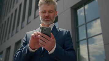 Caucasian senior middle aged employer mature happy businessman receive message offer opportunity retired business man read good news smartphone excited overjoyed celebrate mobile phone victory in city video