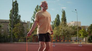 pensionista saltar corda fisiculturista Esportes poder ativo pular praticando mais velho Senior movimento saltando manhã muscular pernas cuidados de saúde exercite-se Treinamento estádio cidade lado de fora atletismo desportista sorrir fino video