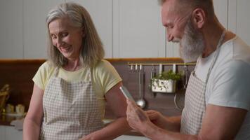 kaukasisch verheiratet alt Senior Paar glücklich Familie reifen im Ruhestand Frau Mann Kochen Frühstück zusammen im Küche Zuhause heiter lächelnd Lachen Mann halt Handy, Mobiltelefon Telefon machen Foto Ehefrau Koch Essen Blog video