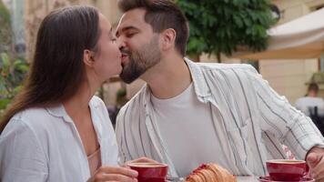 europeu caucasiano casal dentro amor comendo café da manhã dentro cidade cafeteria namorado beijo namorada sorridente riso Diversão harmonia relação prazer afetuoso amoroso homem e mulher em romântico encontro ao ar livre video