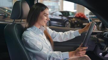 Happy Caucasian woman choose new car in showroom automobile salon looking around touch wheel make decision buy auto female driver woman girl lady smile enjoy sitting in luxury transport vehicle rental video