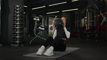 gezond sportvrouw Kaukasisch meisje opleiding sterk armen spier actief training Aan sport- mat in geschiktheid Sportschool sportief vrouw vrouw atleet twist Gooi geneeskunde bal oefenen met uitrusting in sport club video