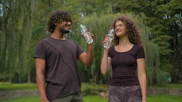 sano indio hombre caucásico mujer bebida en ciudad parque al aire libre multirracial chico niña contento aptitud Pareja deporte personas juntos relajarse pausa descanso sed Bebiendo embotellado agua actualizar bienestar salud video