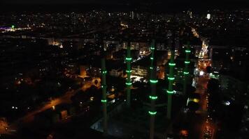 Drone captures Mersin at night, highlighting mosque, cityscape. Night view of Mersin with mosque center frame. Illuminated Mersin, mosque in cityscape, seen from drone at night video