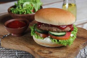 Delicious fresh meat burger with tomato sauce and vegetables served on wooden tray. photo