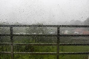Raindrops on window pane with white mist on balcony railing background photo