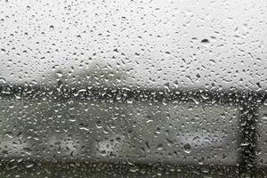 Raindrops on window pane with white mist on balcony railing background photo