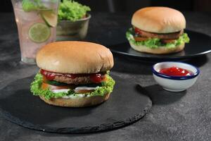 Two delicious fresh meat burgers with tomato sauce and vegetables on a dark background. photo