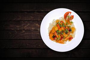 Top view of instant noodles in white bowl with added vegetables and sausage pieces on dark wooden background. photo