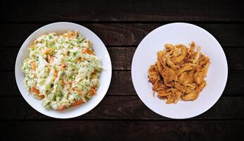 Side dishes, sweet chicken cutlet dish and coleslaw are on white plate on dark wooden background, top view. photo