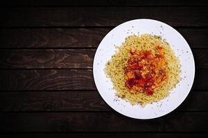 Top view of instant noodles in white bowl with tomato and egg vegetable topping on dark wooden background. photo