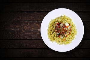 Top view of instant noodles in white bowl with added garlic and chili on dark wooden background. photo