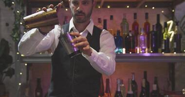 Professional barman in a white shirt and black apron throwing liquid with steel shaker. Shot in RED camera 4K in slow motion video