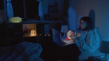 Young girl watching a movie eating popcorn with her laptop in bed at night. Slow motion RED camera 4K video