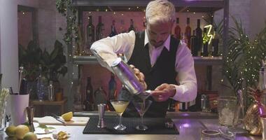 bonito jovem profissional barman dentro uma branco camisa e Preto avental fazer coquetel dentro noite clube festa em Barra contador. vermelho Câmera video