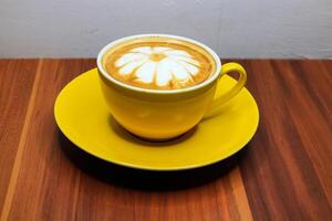 Coffee latte art flowery in yellow cup on wooden background. photo