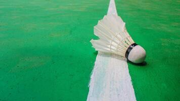 The badminton shuttlecock falls over the white line against the green field background. photo