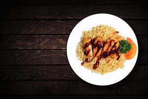 Top view of instant noodles in white bowl with added pieces of chicken on dark wooden background. photo