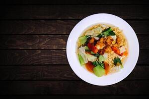 Top view of instant noodles in white bowl with vegetable toppings on dark wooden background. photo
