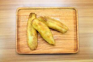 Three fried bananas are placed on a wooden tray photo