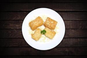 Four pieces of crispy fried cassava with a sprinkling of cheese are served on a white plate against a dark wood background. photo