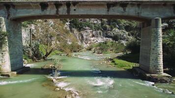 Drone flies under bridge, capturing mountain river, bridge, mountain river scenery, and bridge over mountain river. Showcases engineering, natural beauty video