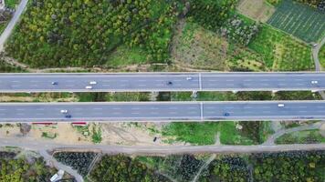 Drone view of traffic on two-lane highway crossing green fields under a blue sky. Aerial footage showcases two-lane highway, cars moving through the landscape video