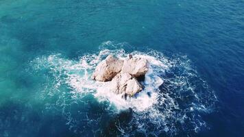 Drone captures island rock in tranquil sea, waves wash over. Clear blue sea surrounds island, rock visible. Island, rock stands out, serene sea background. video