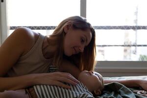 mother and newborn baby are lying on the bed in the bedroom opposite the window photo