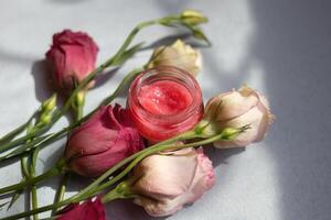 jar with cosmetic cream surrounded by fresh eustoma flowers on a gray background top view photo