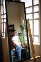 young beautiful pregnant woman looks in a large mirror while standing in her authentic vintage apartment photo