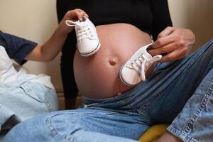 mom and daughter put white sneakers for a newborn on a big tummy. close-up shot photo