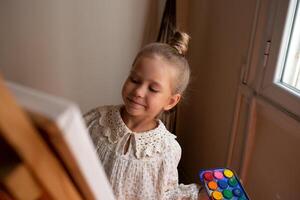 little cute girl draws with paints on canvas at the easel photo