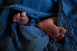 legs of a newborn baby in a blue muslin swaddle. close-up shot photo