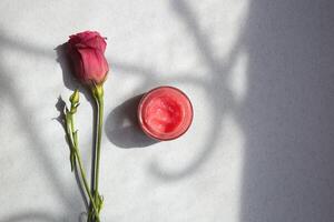 jar with cosmetic cream surrounded by fresh eustoma flowers on a gray background top view photo