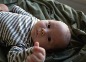 mixed race newborn baby lies wrapped in a green muslin swaddle photo