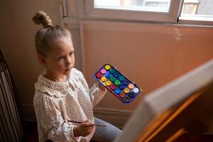 pequeño linda niña sorteos con pinturas en lona a el caballete foto