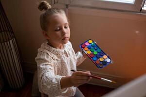 little cute girl draws with paints on canvas at the easel photo