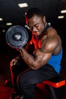 African american bodybuilder man with strong man and muscular torso. Male wearing sport clothes isolated on dark gym background. photo