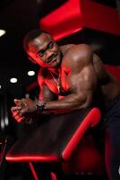 Trained and pumped up athlete rests on bench in modern gym. Dramatic law key red lightning. Portrait of a bodybuilder. photo