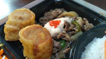 Japanese Rice dish containing rice, beef teriyaki, salad and dressing, and fried snacks photo