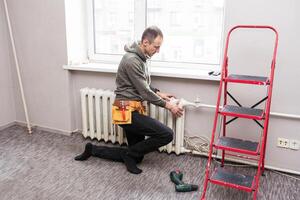 Worker replaces domestic radiator in the living room photo
