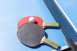 Red and black Table Tennis Paddles and ball on the blue table tennis table with net. Ping Pong concept with copy space photo